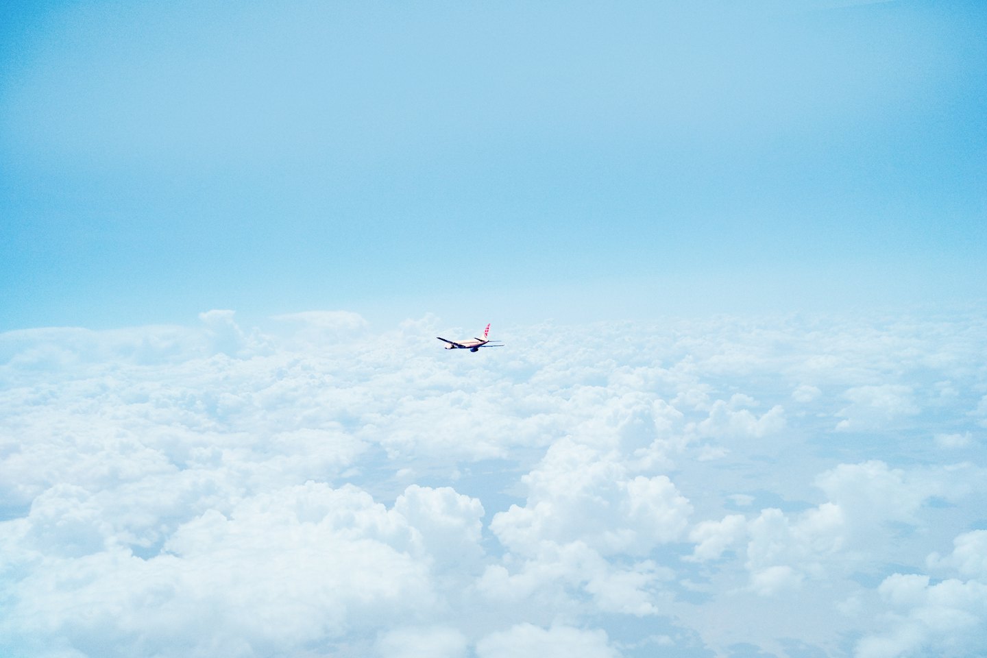 Passenger jet flying over white clouds in blue sky.