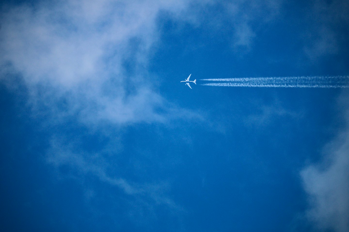 A white airplane leaves a long contrail across a blue sky.